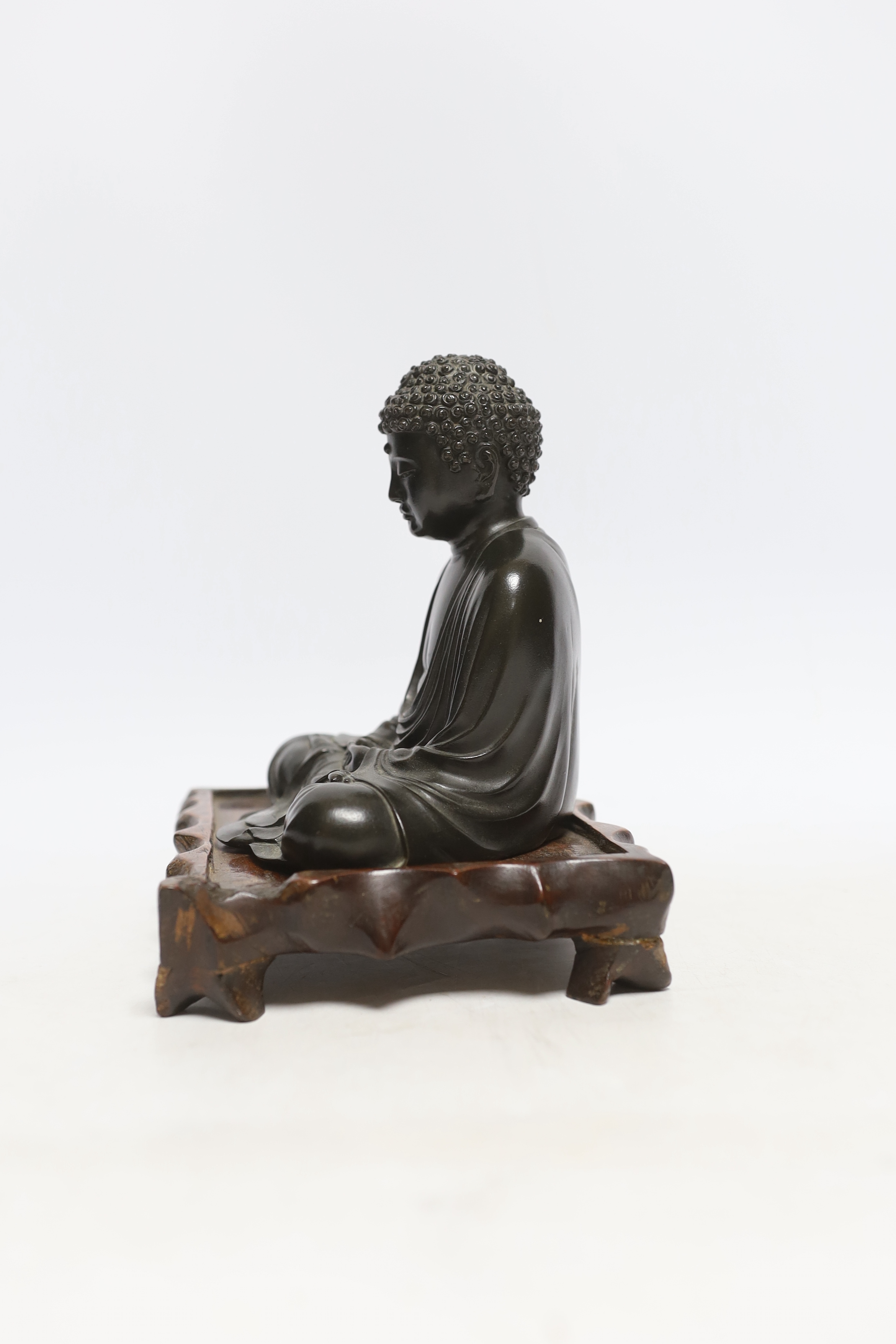 A Japanese bronze figure of Buddha, Meiji period, inscribed seven character mark to base, on a hardwood stand, 15cm high